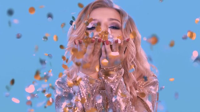 Close-up of a beautiful blonde inflates the confetti from the flappers that lie on her palms. He looks into the camera.