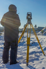 A surveyor with an assistant makes a topographical survey for the cadastre at a construction site in winter