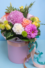 beautiful floral arrangement in the box, pink and yellow rose, pink eustoma, green and pink chrysanthemum, white carnation, pink dahlia on a blue, turquoise background with space for text