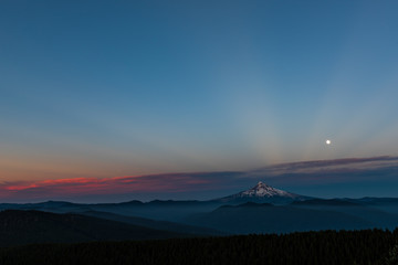 Obraz premium the last rays of sunshine streak through the sky with the full moon sitting over a mountain