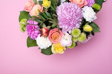 beautiful floral arrangement in the box, pink and yellow rose, pink eustoma, green and pink chrysanthemum, white carnation, pink dahlia on pink background with space for text.