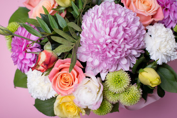 beautiful floral arrangement in the box, pink and yellow rose, pink eustoma, green and pink chrysanthemum, white carnation, pink dahlia on pink background with space for text.