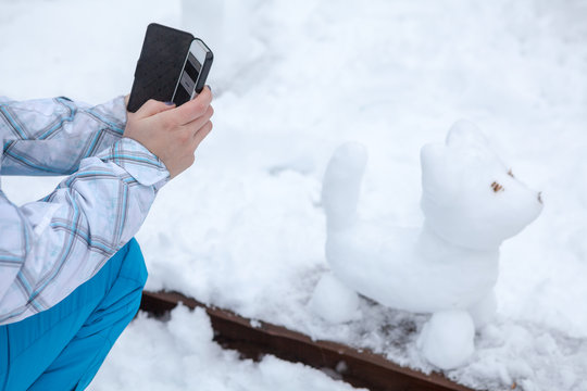 Human hands photographs snowman the dog on cell phone in park at winter