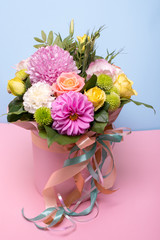 Naklejka premium beautiful floral arrangement in the box, pink and yellow rose, pink eustoma, green and pink chrysanthemum, white carnation, pink dahlia on pink, blue background with space for text.