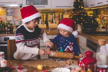 Sweet toddler child and his older brother, boys, helping mommy preparing Christmas cookies at home