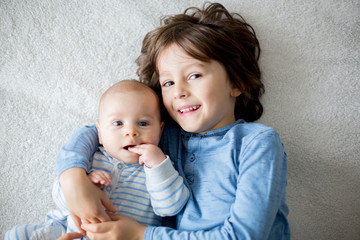 Happy brothers, baby and preschool children, hugging at home on white blanket