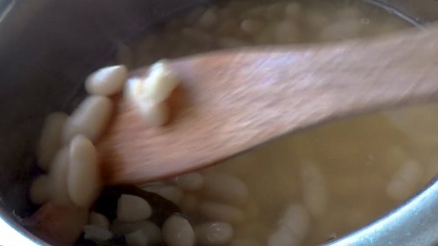Slow cooking of the beans. With a wooden pole beans are mixed with dry bay leaves and garlic poached