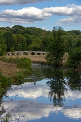 Obraz premium Sky and trees reflected in pond with arch bridge in background