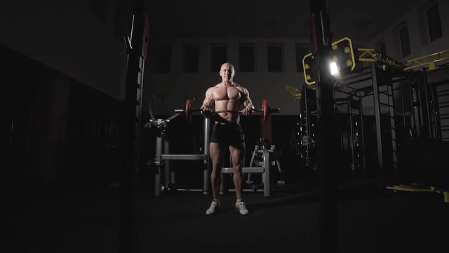 Weightlifter lifts barbell to training biceps. Bodybuilder doing exercise with barbell in dark gym. Exercises for muscles of biceps in slow motion