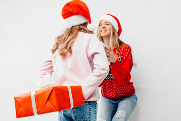 Mom and daughter celebrate the New Year, in Santa hats and Christmas sweaters, give each other Christmas presents,