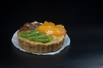 fruit tart stacked high with kiwi peach grape dark background.