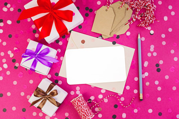 Fototapeta na wymiar Gift box with ribbon, christmas decor and clean notebook with pencil on pink background with confetti.