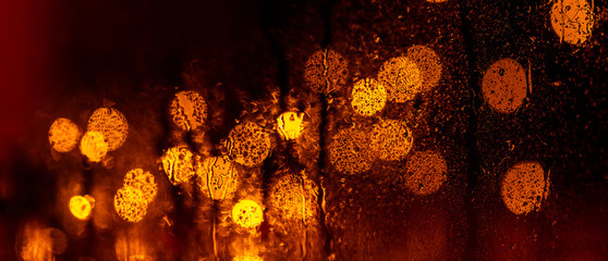glare of the night city through the window in the drops of rain