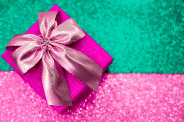 Pink gift box with a bow on a color sparkling background.