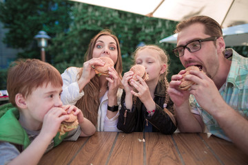 hungry family eating hamburgers, sitting at a table in a fast food restaurant