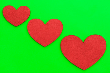 Three hearts of different sizes of red color on a green background. Concept on the theme of love for Valentine's Day.