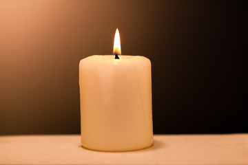 Large lighted candle on a shade background.