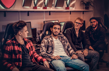 A team of multiracial teenage gamers sitting on gamer chairs and looking at a camera in a gaming club or internet cafe. © Fxquadro