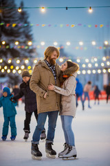 Young couple in love Caucasian man with blond hair with long hair and beard and beautiful woman have fun, active date skating on ice scene in town square in winter on Christmas Eve © Elizaveta