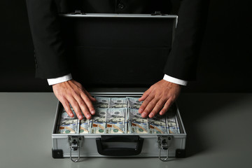 Businessman with suitcase full of money on dark background