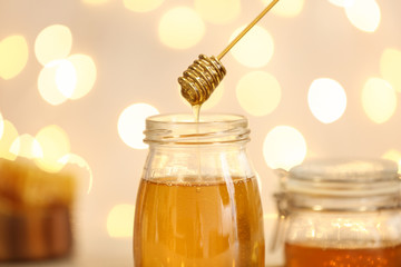Honey dripping from dipper into jar against blurred lights, closeup
