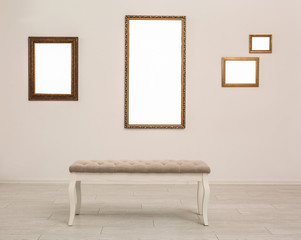 Frames with empty canvases on wall and bench in modern art gallery. Mockup for design