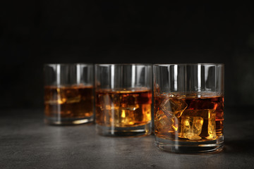 Golden whiskey in glasses with ice cubes on table. Space for text