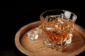 Golden whiskey in glass with ice cubes on wooden barrel. Space for text © New Africa