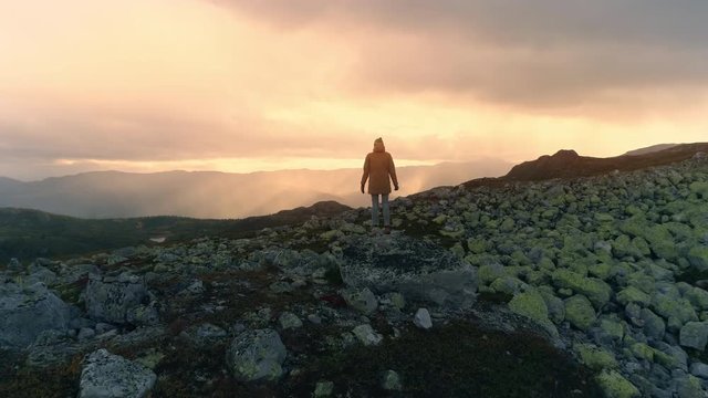 Woman standing on rock on top of the high mountain looking epic view in Norway at sunset aerial shot