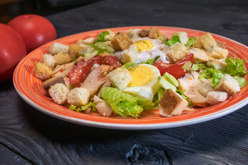 Caesar salad in red plate. Caesar salad consists of roasted chicken breast, iceberg lettuce, tomato, parmesan cheese. Popular dish of European cuisine and cuisines of other countries.