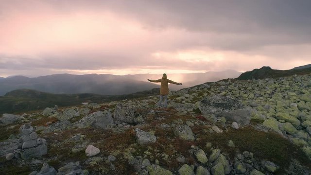 Woman imitate flying on top of the high mountain in Norway at sunset