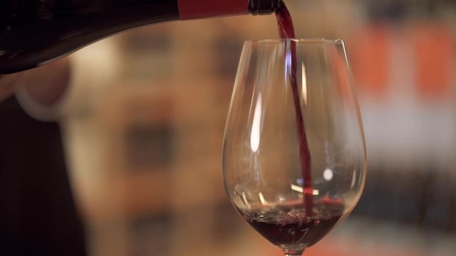 Slow pouring red wine into a wine glass. Female hand pours wine into a wine glass close up.