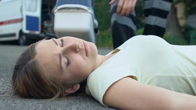 Unconscious woman lying on asphalt, paramedic rendering first medical assistance