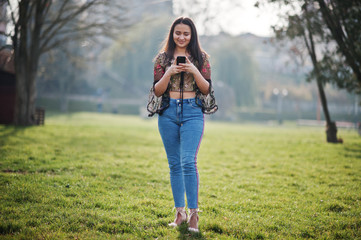 Pretty latino model girl from Ecuador wear on jeans posed at street with mobile phone.