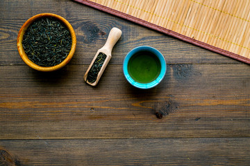 Chinese tea concept. Tea ceremony. Dry tea leaves in bowl and wooden scoop near cup of tea on rustic wooden background and bamboo table mat top view space for text
