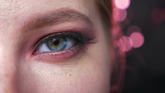 Focused amazing blue eye in rowing pink eyeshadows looking at camera chill, pure beauty of model on black background indoors