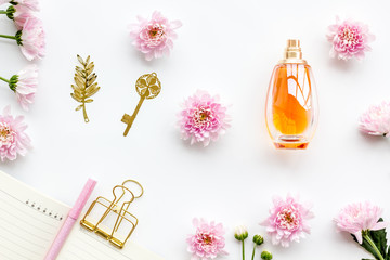 Perfume on feminine desk. Women's accessories. Perfume near notebook for dairy, vintage key among flowers on white background top view