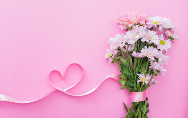 Obraz na płótnie Canvas daisy bouquet and heart shaped ribbon, on pink background