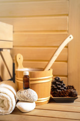 small private Finnish sauna setting with water bucket, oil essence, cones, hot stones and white towel on wooden background. wellness spa concept relax and treatment therapy. Close up, selective focus