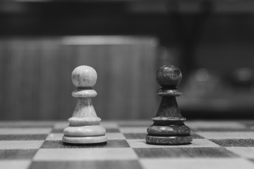 Standoff of black and white. Two wooden figures on chess board near each other. Pawns battle. Handmade old chess.