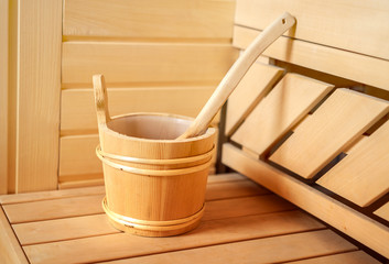 Fototapeta na wymiar small private Finnish sauna setting with water bucket, oil essence, cones, hot stones and white towel on wooden background. wellness spa concept relax and treatment therapy. Close up, selective focus