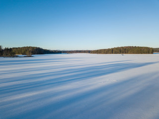 Aerial view on the texture of snow with shadow from trees on the surface of a winter lake 