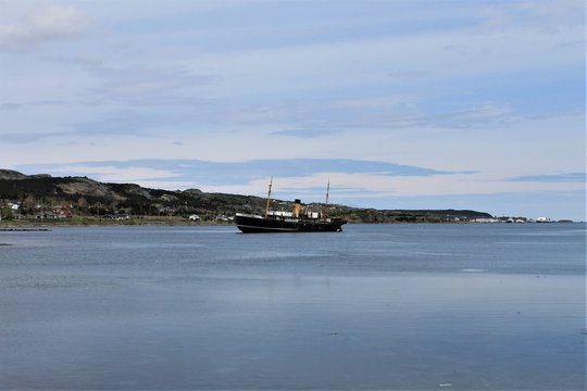Looking across the harbor at the old grounded ship, the Kylie, Harbour Grace, Newfoundland and Labrador, Canada. Panoramic view of the harbor, and the town. Large expanse of blue water and blue sky.