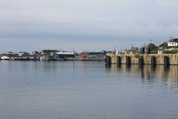 Fototapeta premium View of Port Aux Basque Newfoundland, looking across the harbor from the ferry dock. Calm water, overcast sky, a couple of fishing boats tied up dockside.