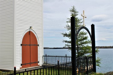 Iron gate and fence around Holy Redeemer Church, Spanards Bay, Newfoundland. View of steeple exit. View of the bay in the background.