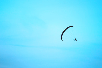 Paraglider silhouette flying in a bright blue sky