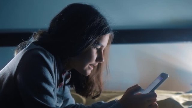 girl teenager and smartphone. little teen hood girl writes a message chatting in social media messenger night evening indoors smartphone on the bed. children technology and communication concept