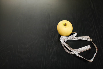 yellow apple with white measuring tape on dark black wooden table.