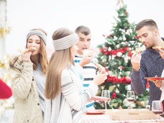 Young friends eating Pizza together on balcony for Christmas