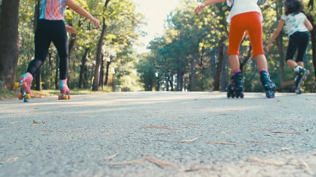 Three girls kids riding rollerblades skating in a park playground, 4k slow motion